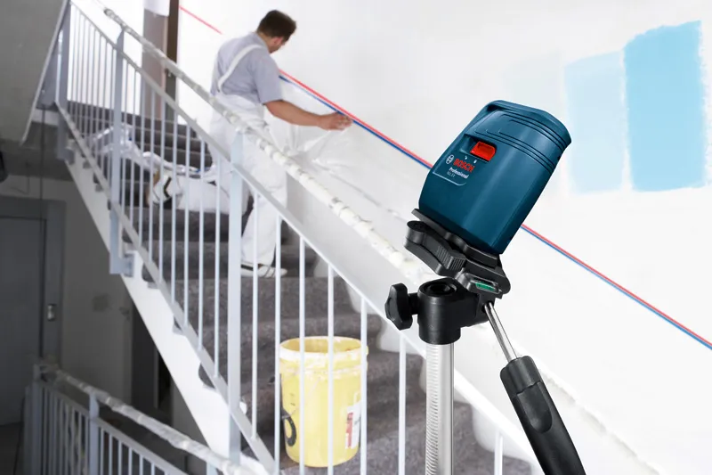 Laser leveling tool projects lines on a stairway wall while a person prepares the surface.