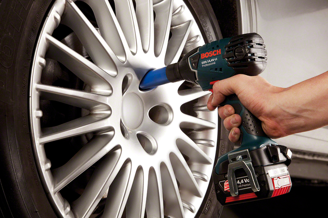 Person uses a cordless impact wrench to tighten bolts on a car wheel.