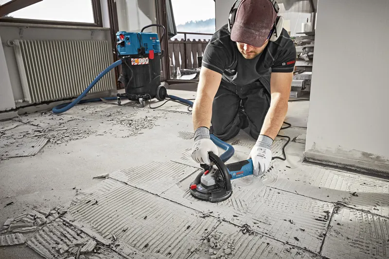 A person wearing safety equipment grinds concrete flooring with a concrete grinder.