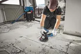 A person wearing safety equipment grinds concrete flooring with a concrete grinder.