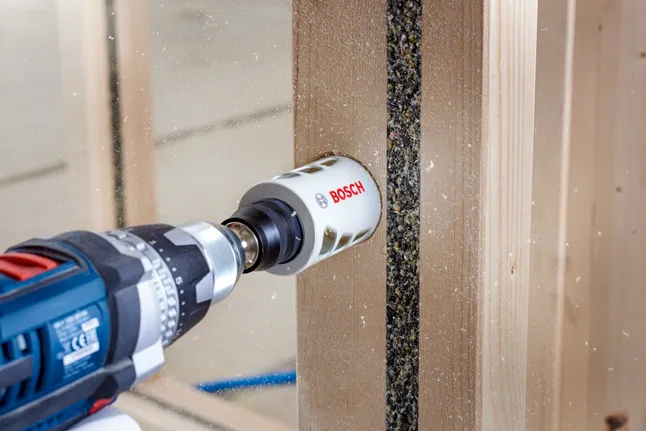 Hole saw drilling a circular opening through laminated wood panel.