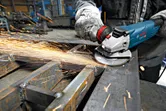 A person wearing safety equipment grinds metal, producing bright sparks.