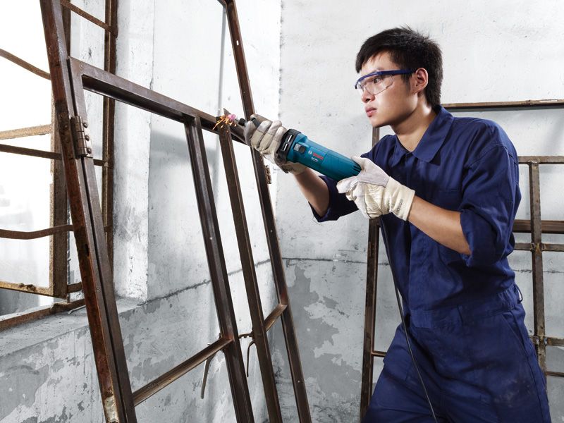 Person wearing safety equipment uses a straight grinder on a metal window frame.