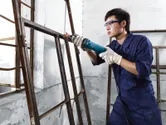Person wearing safety equipment uses a straight grinder on a metal window frame.