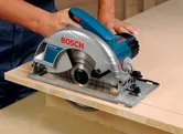 A person cuts plywood using a handheld circular saw.