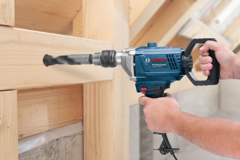 A person operates a power drill to bore a hole through a wooden beam.