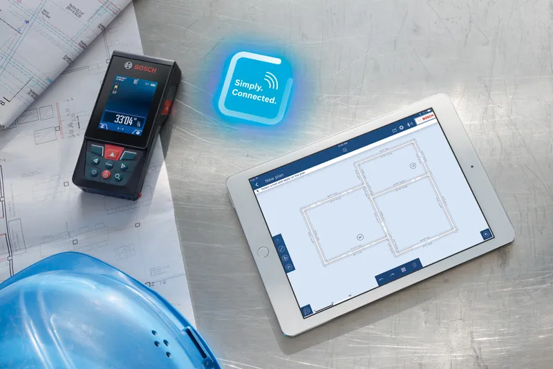 Laser measure beside blueprints and a hard hat, with a tablet displaying floor plans.