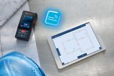Laser measure beside blueprints and a hard hat, with a tablet displaying floor plans.