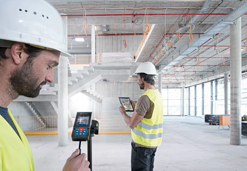 Person wearing safety equipment uses a laser measure in a building under construction.
