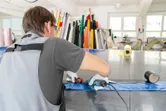A person wearing safety equipment uses a heat gun to seal plastic sheets on a worktable.