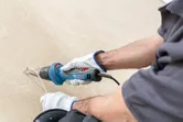 A person wearing safety equipment uses a heat gun to strip material from a surface.