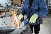 A person wearing safety equipment grinds metal with a cordless angle grinder.