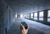 Person using a laser measure to determine distance in an unfinished concrete room.