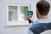 Person using a thermo camera to inspect a window from outside a building.