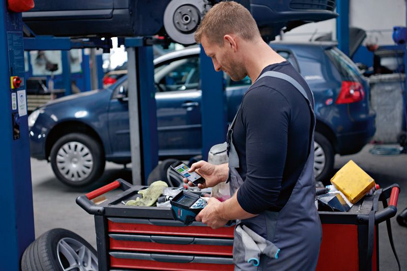 A person wearing safety equipment uses a thermo camera while working in an auto repair shop.