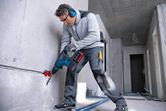 A person wearing safety equipment drills into a concrete wall in a construction area.