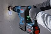 A person wearing safety equipment drills into a concrete wall with a cordless rotary hammer.