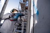 Person wearing safety equipment drills into a concrete wall at a construction site.