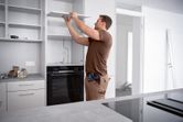 A person installs a kitchen shelf using a cordless screwdriver.