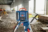 Laser leveling tool set on a tripod at a construction site, person wearing safety equipment in background.