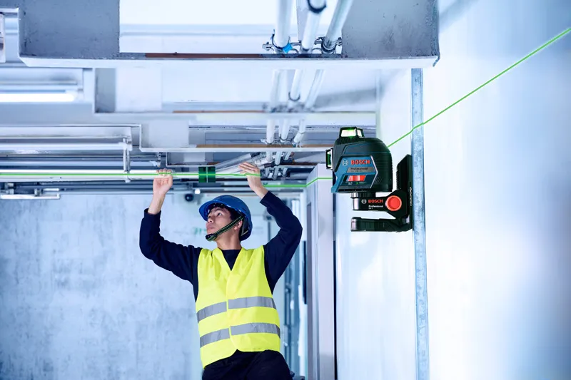 A person wearing safety equipment aligns pipes using a green laser leveling tool.