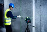 A person wearing safety equipment aligns tiles on a wall using a laser leveling tool.