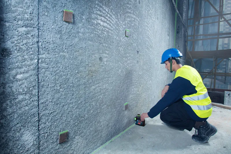 A person wearing safety equipment aligns marks on a wall using a laser leveling tool.