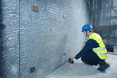 A person wearing safety equipment aligns marks on a wall using a laser leveling tool.