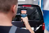 A person uses a thermo camera to scan the rear window of a black van.