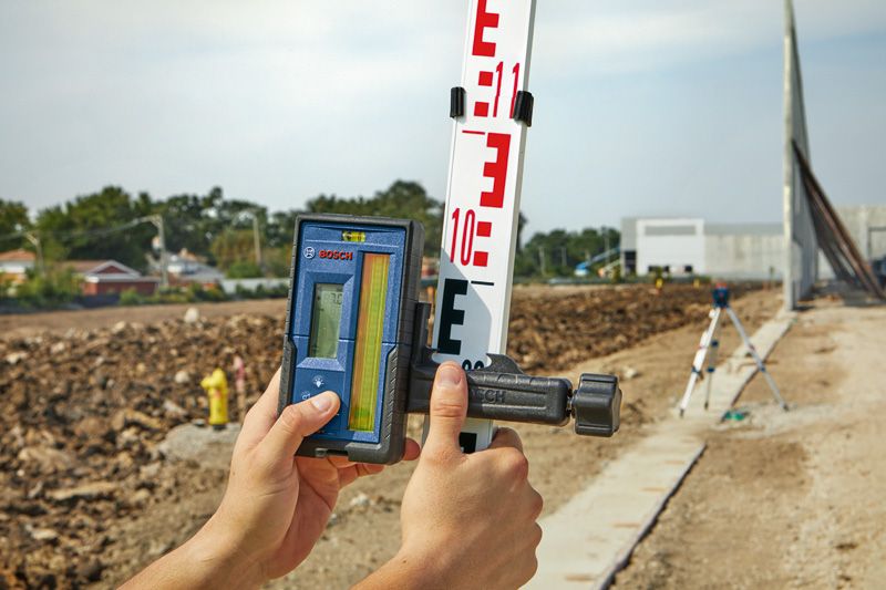 Person holding a laser receiver against a leveling rod at a construction site.