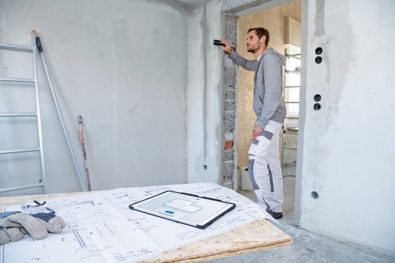 A person uses a laser measure to check wall distance at a construction site.