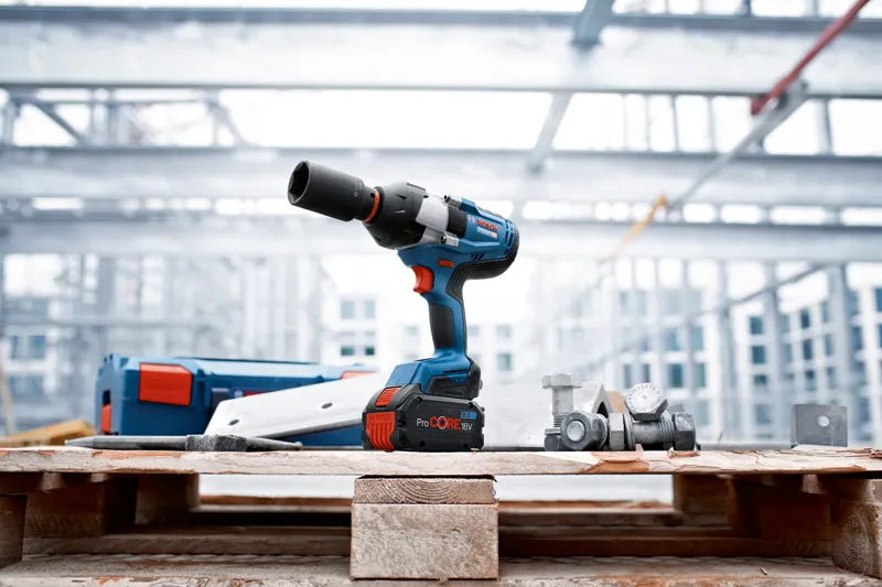Cordless impact wrench resting on a wooden pallet beside bolts at a metal construction site.
