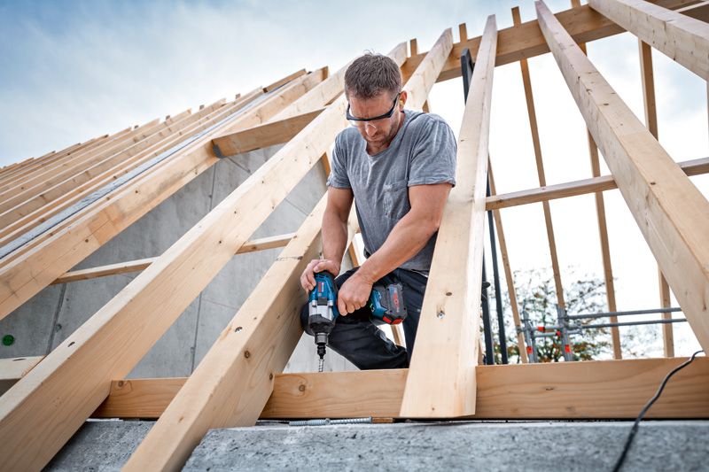 A person wearing safety equipment fastens a wooden beam with a cordless impact wrench.