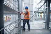 A person wearing safety equipment fastens a bolt to a steel beam with an impact wrench.