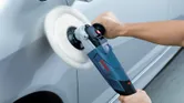 A person uses a polisher to buff the surface of a car.