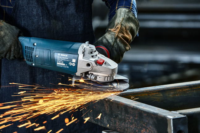 Person wearing safety equipment grinds metal, producing bright sparks.