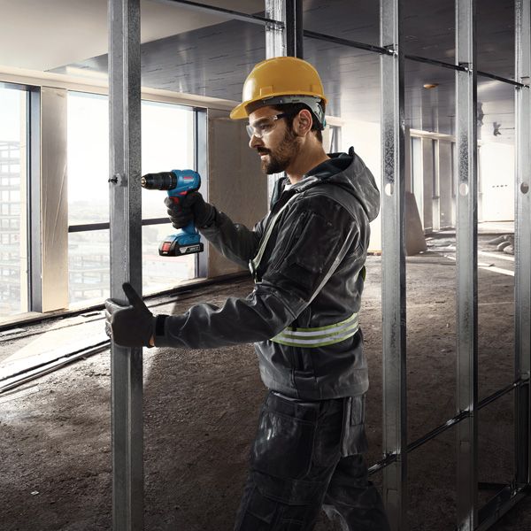 A person wearing safety equipment uses a cordless drill on a metal wall frame.