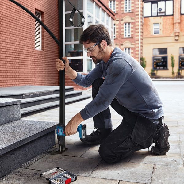A person wearing safety equipment drills a hole to install a metal handrail on stone steps.