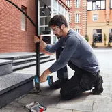 A person wearing safety equipment drills a hole to install a metal handrail on stone steps.