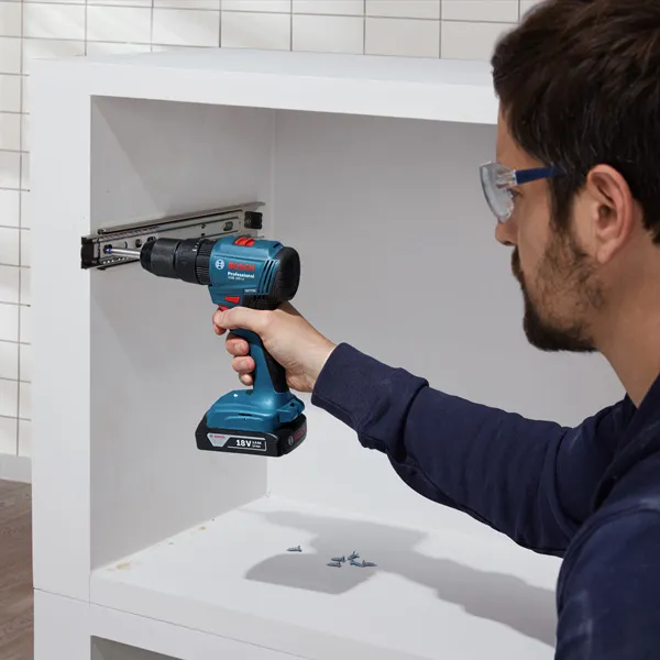 A person wearing safety equipment uses a cordless drill to install a cabinet rail.