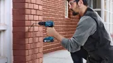 Man drilling into brick wall.
