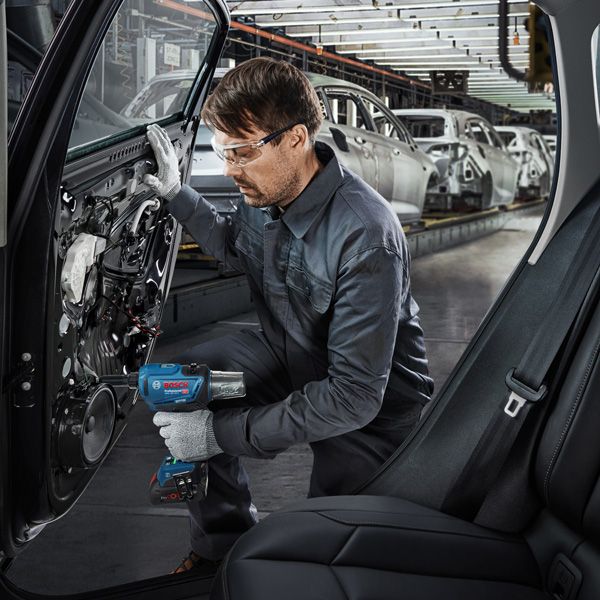 A person wearing safety equipment uses a power tool to assemble a car door in a factory.
