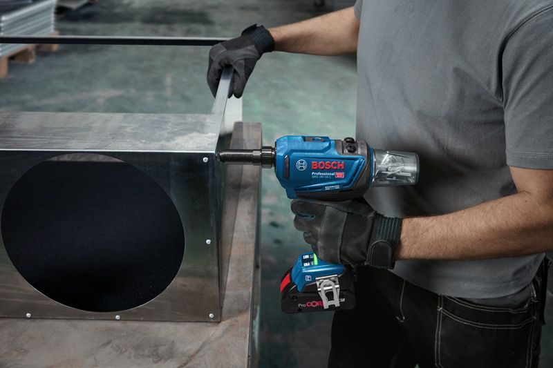 A person wearing safety equipment uses a cordless impact wrench on a metal duct.