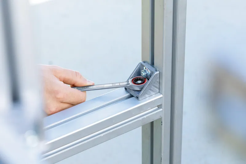 A person tightens a bolt on a metal frame using a spanner.