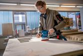 A person wearing safety equipment sands a wooden surface with a random orbit sander.