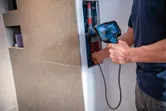 A person uses an inspection camera to examine pipes inside a wall opening.