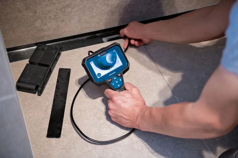 A person inspects a narrow floor space using an inspection camera device.