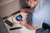 A person inspects inside a narrow wall space using an inspection camera.