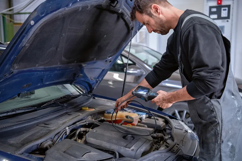 A person inspects a car engine using an inspection camera in a workshop.