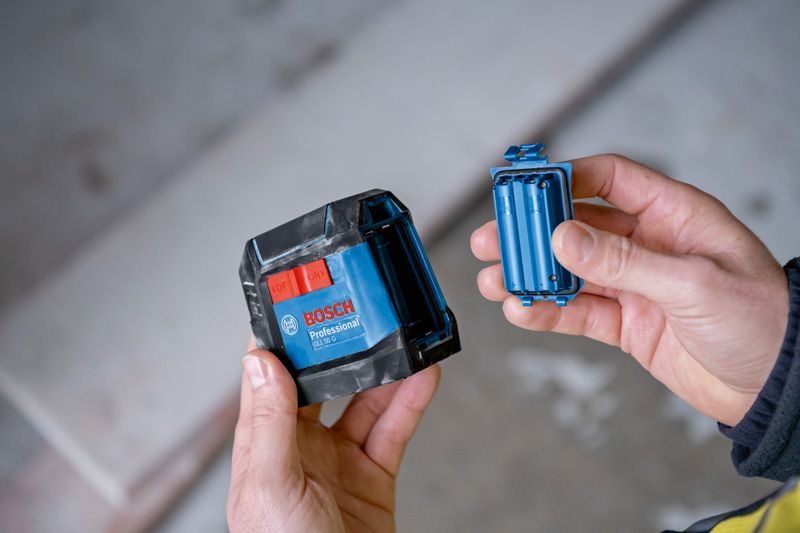 Person holds a blue laser leveling tool and its battery compartment indoors.